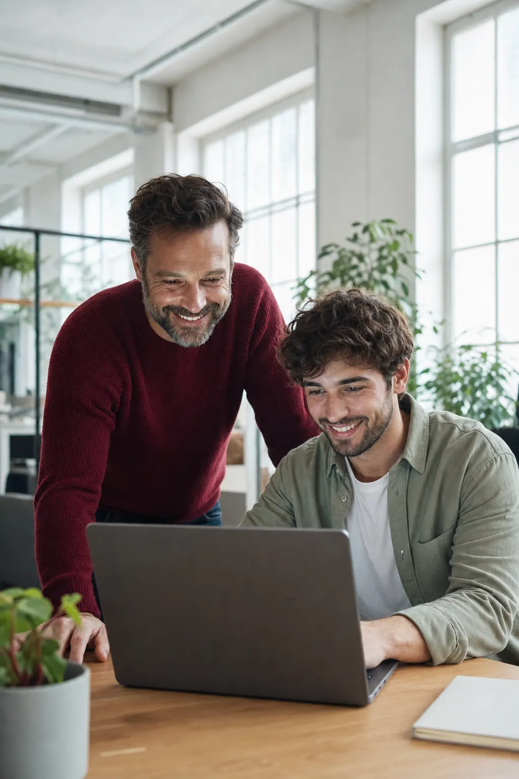 Zwei begeisterte Software-Engineers arbeiten gemeinsam an einem Laptop in einem hellen, modernen Büro